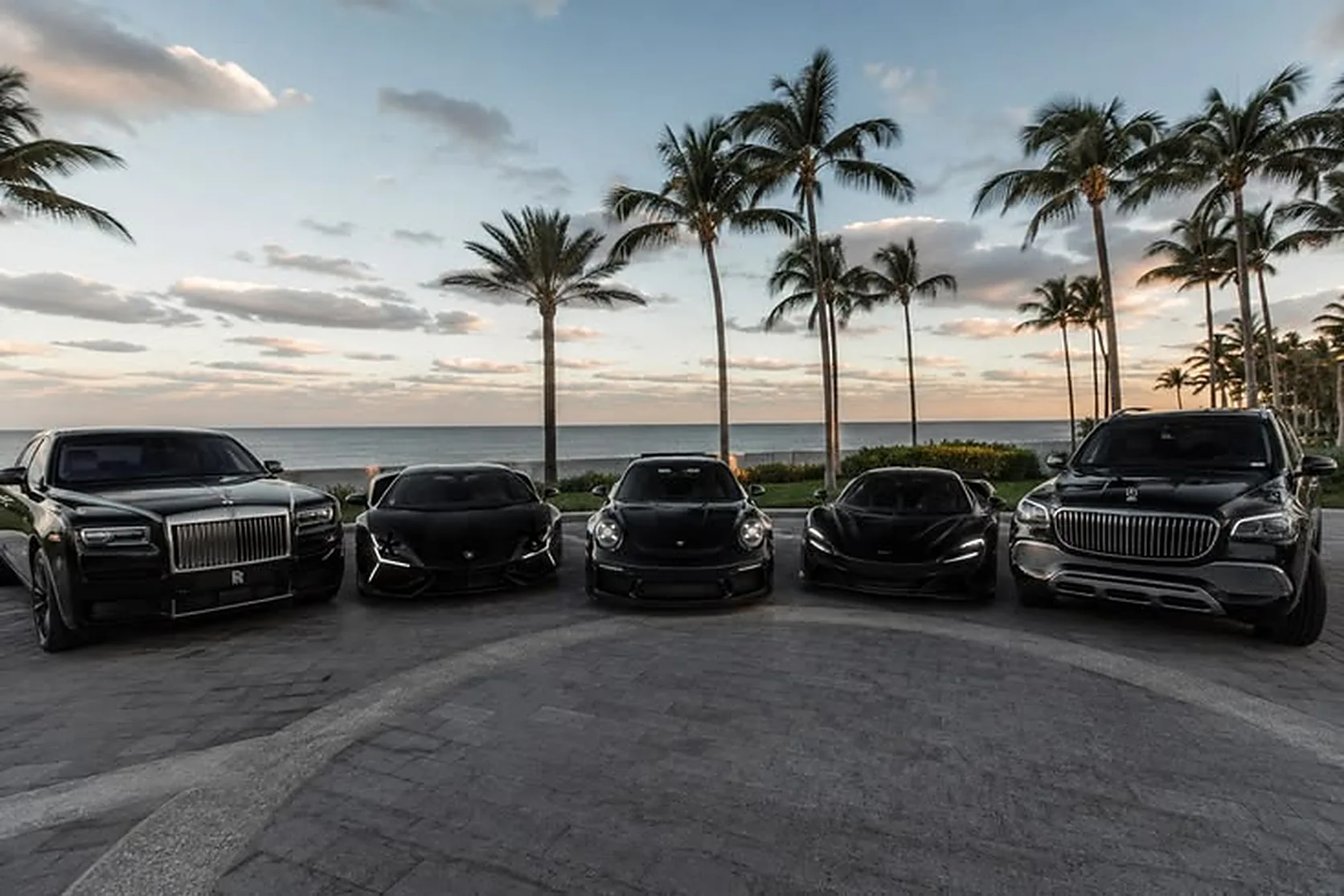 Black Rolls-Royce, Lamborghini, Porsche, McLaren and Mercedes-Maybach lined up by the sea at sunset in Dubai